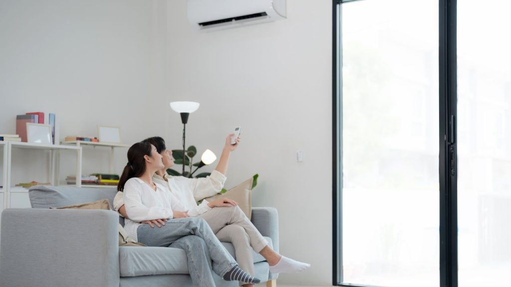 a happy couple on a couch turning on the air conditioning unit